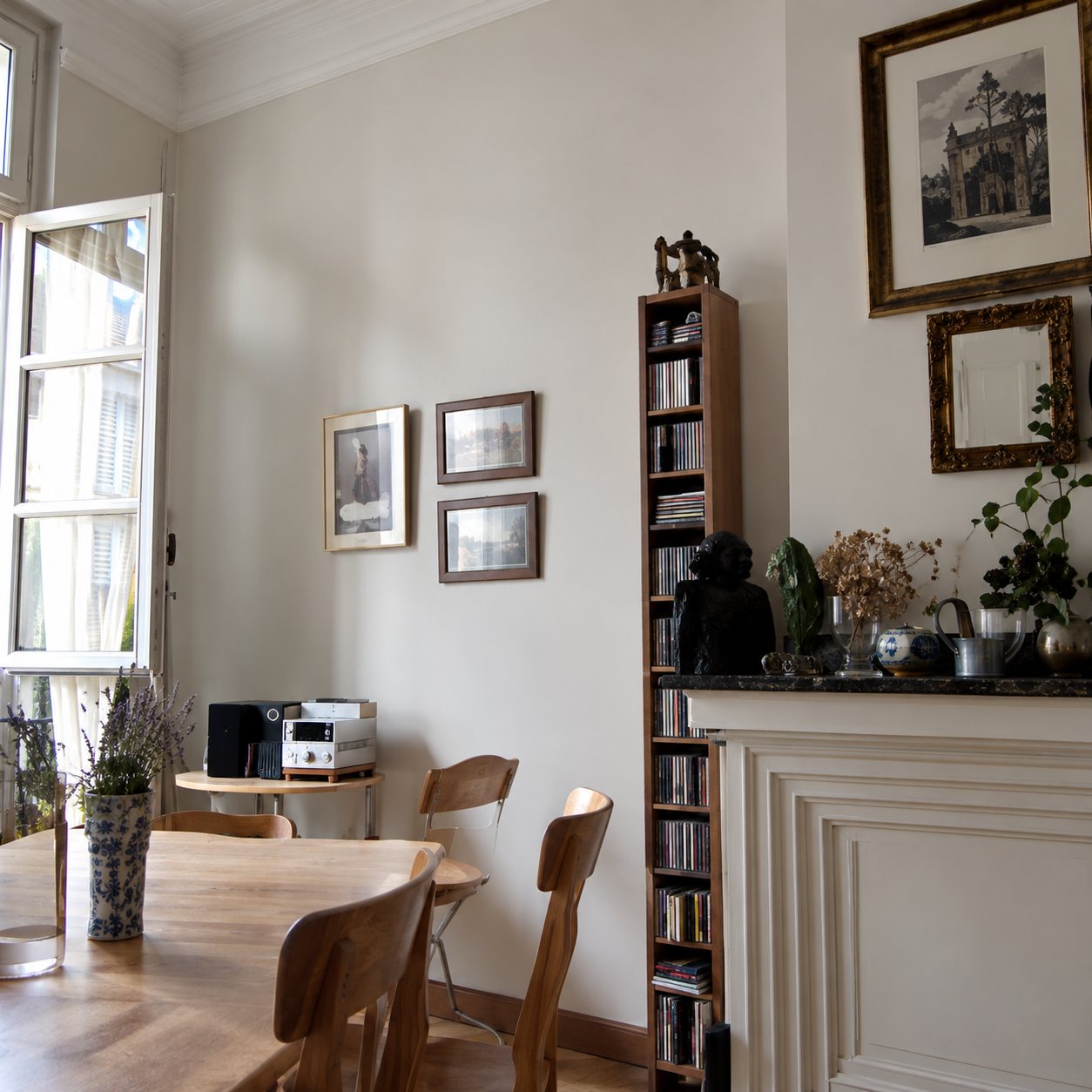 Photo en noir et blanc d'un salon clair avec une fenêtre ouverte, une table, une bibliothèque remplie et une cheminée ornée d'un miroir.
